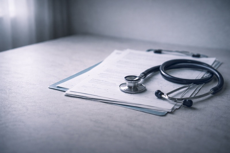 Stéthoscope posé sur des documents médicaux partiellement visibles, avec un espace vide suggérant les non-dits du monde médical autour des effets secondaires des traitements de la sclérose en plaques.