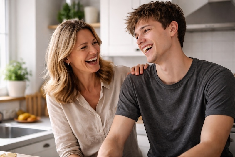 moment-legerete-mere-jeune-adulte-sp Mère et jeune adulte rient ensemble dans une cuisine, partageant un moment de légèreté et de complicité.