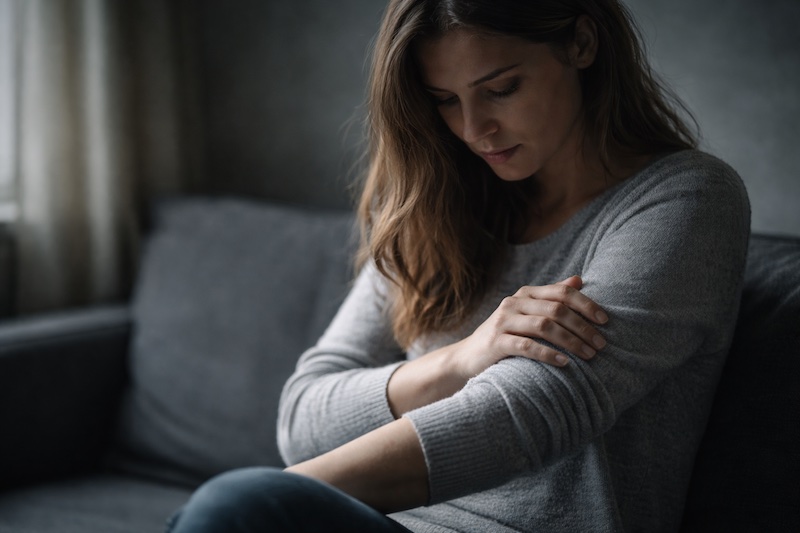 verifier-sensations-anxiete-sp Femme touchant son bras avec inquiétude, regard concentré sur ses sensations corporelles, illustrant l’hypervigilance et l’anxiété fréquentes après un diagnostic de sclérose en plaques.