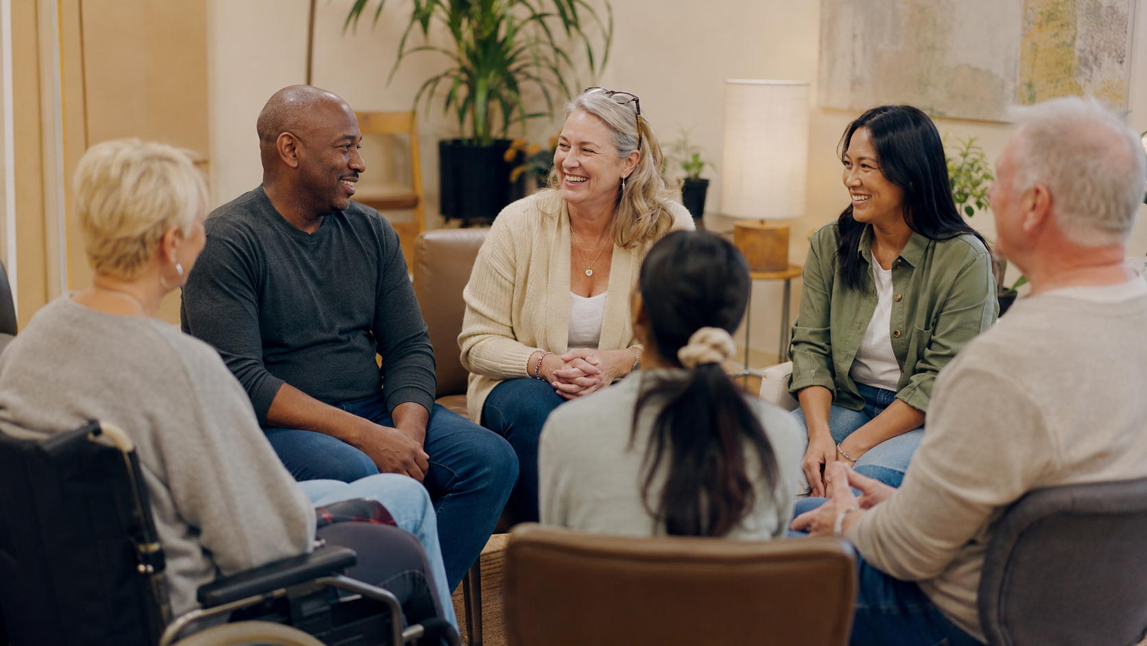 groupe-soutien-sp Groupe de personnes assises en cercle, échangeant avec des sourires naturels, illustrant le soutien communautaire pour les personnes atteintes de sclérose en plaques.
